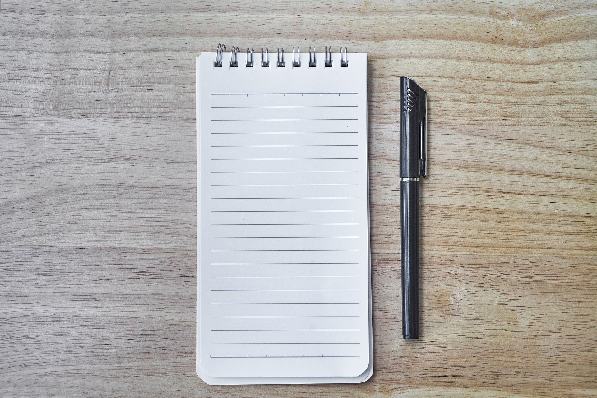 a blank notebook on a wooden table with a pen next to it