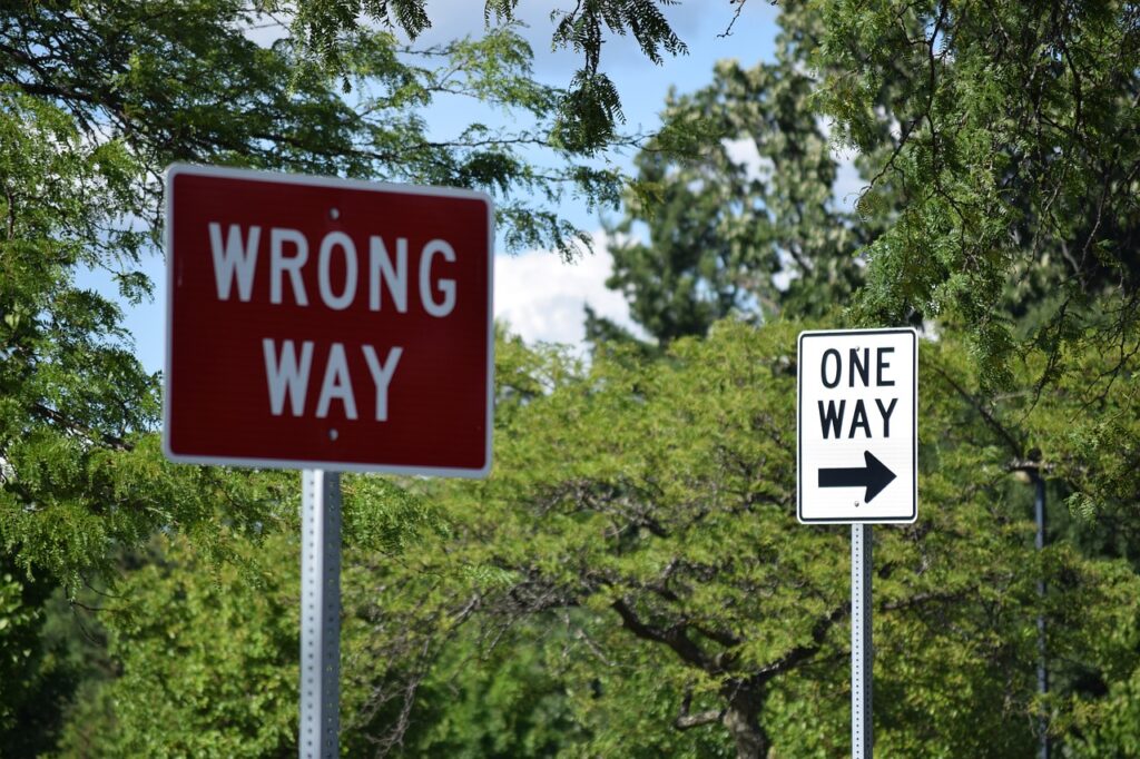 Two road signs, one saying "wrong way" and the other saying "one way"