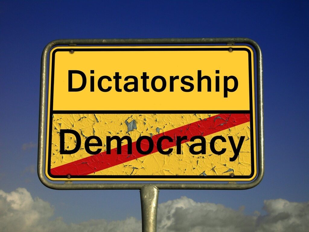 Sign saying the word "Dictatorship" in fresh paint above the word "Democracy" with a line through it and in weathered paint