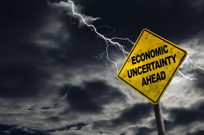 A weathered sign proclaiming Economic Uncertainty against a background of stormy lightning. 